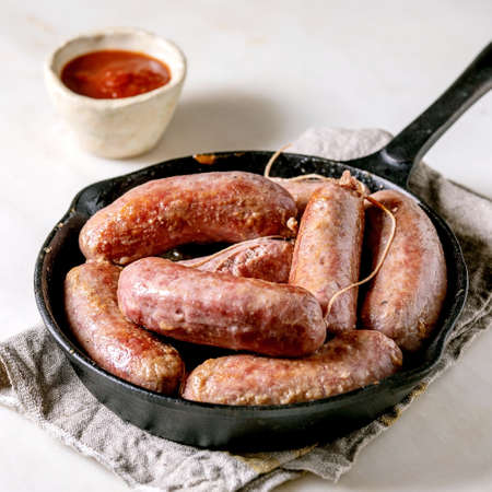 Grilled italian sausages salsiccia in cast-iron pan on cloth napkin over white marble table. Square imageの写真素材