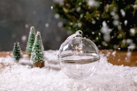 Christmas or New Year greeting card. Glass transparent empty opening ball for gift or products display, decorative Christmas trees on snow and fir tree at background. Xmas holidays advertising conceptの写真素材