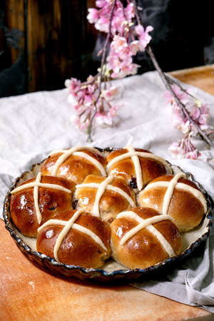Homemade Easter traditional hot cross buns on ceramic dish with blossom flowers over orange stone...