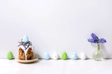 Homemade traditionla Easter kulich cake with chocolate nest and eggs on plate standing on white...