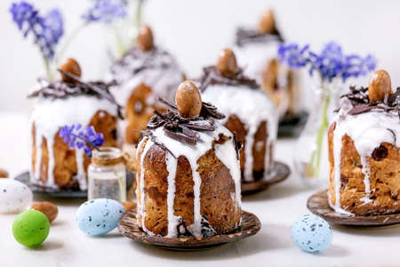Homemade traditionla small Easter kulich cakes with chocolate nests and eggs on plates decorated...