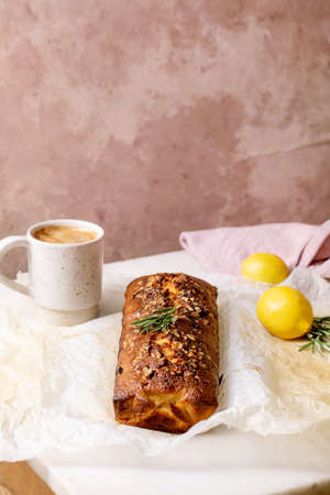 Homemade lemon cake with nuts and rosemary on crumpled baking paper, serving with fresh lemon and coffee mug on white marble table.の写真素材