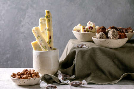 Variety of homemade toffee chocolate almond nuts candy, dark chocolate truffle, white chocolate candy bar in bowls on linen table cloth. Handmade food sweet gifts for any holidays. Sweet tableの写真素材