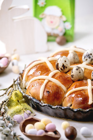 Homemade Easter traditional hot cross buns in ceramic dish with blossom flowers, chocolate candy and...