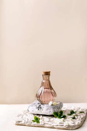 Elegance pink transparent bottle of perfume with cork, standing on textured stone on white marble table with small white flowers Kalanchoe around. Perfume making concept with place for design labelの写真素材