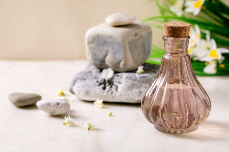 Beautiful pink transparent bottle of perfume with cork, standing with textured stone on white marble table. Small white flowers, spring daffodils. Perfume making concept with place for design labelの写真素材
