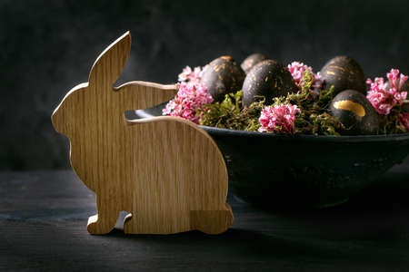 Black Easter concept. Bio colored black eggs with golden spots laying on wild moss with small pink...