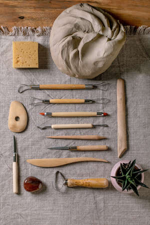 Set for pottery hobby. Piece of raw grey clay and kit of pottery ceramics tools in row on linen...