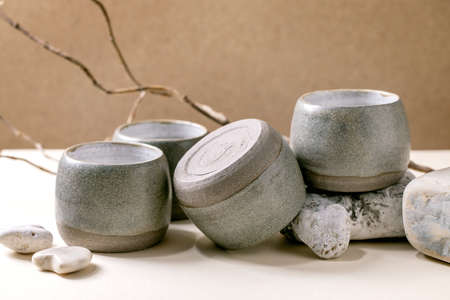 Set of empty grey texture craft ceramic cups with dry branch and stones standing on table. Brown...