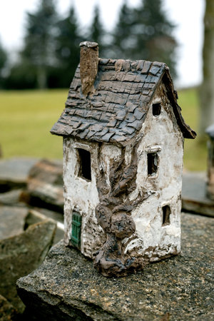 New trends in garden and interior decoration: ceramic house with old tree in modern style. Garden ceramics, miniature. The house placed on old stone wall against rural landscape. Cloudy day.の写真素材
