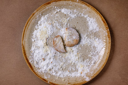 Last broken cookie. Homemade shortbread cookie dusted with powdered sugar on large ceramic pale....