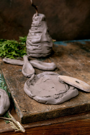 Pottery workshop idea for children and adults: ceramic crafts made of raw clay using coil technique, handmade vase, plate, spoons. Thuja branches and tools on a dark wooden table.の写真素材