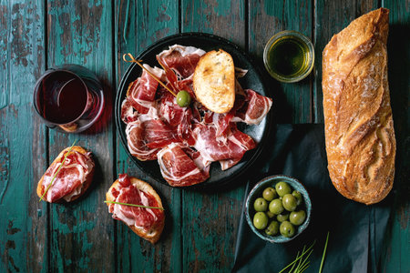 Sliced Spanish ham Jamon Iberico paleta on black plate. Bowl of green olives, fresh and toasted...