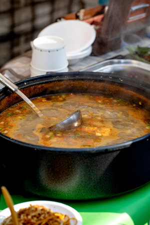 European street food festival. Large pot traditional tomato soup displayed counter with ladle inside. Rich red homemade soup hungry ready serving festival visitors outdoor market atmosphere.の写真素材