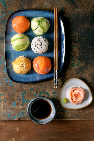 Temari sushi. Trendy sushi balls with salmon, avocado, cucumber, and Japanese omelet on blue plate. Soy sauce, pickled ginger, chopsticks on rustic wooden table. Top viewの写真素材
