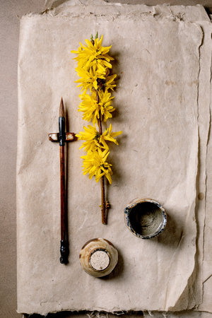 Artistic composition yellow forsythia branch wooden calligraphy pen ink pot on vintage mulberry paper. Flat lay minimal aesthetic for creative workspace concept.の写真素材