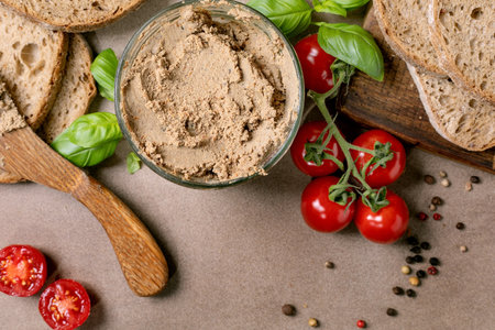 Top view homemade liver pate glass bowl fresh bread slices cherry tomatoes basil leaves wooden spoon rustic background. Healthy appetizer snack.の写真素材