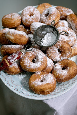 Homemade donuts covered powdered sugar plate with small metal sifter. Fresh baked sweet pastries dusted with icing sugar traditional dessert.の写真素材