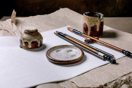 Traditional Chinese calligraphy tools arranged on white rice and mulberry paper. Ceramic inkwell ink stone brushes with wooden handles for oriental painting writing practice.の写真素材