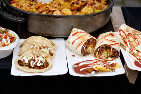 Delicious Mexican street food display with beef tacos burritos nachos and frying pan with potato mix. Authentic cuisine served on disposable plates with sauce.の写真素材