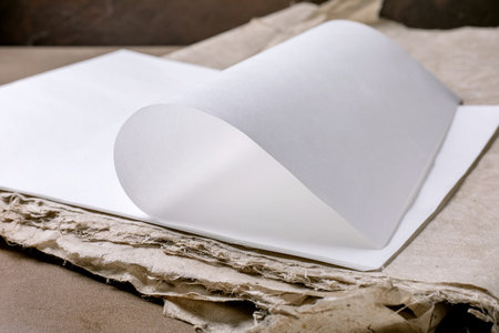 Closeup blank white rice and mulberry paper sheet with curled page on recycled cardboard background. Minimalist composition with clean paper and textured ecofriendly materials.の写真素材
