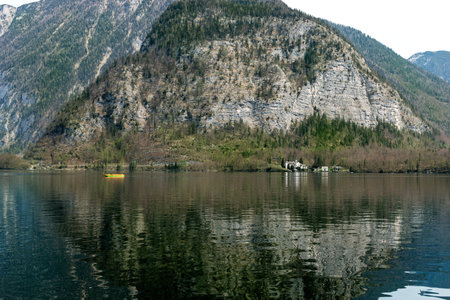 Tranquil alpine lake with crystal clear water reflecting majestic mountain. Small yellow boat adds a vibrant accent to serene landscape. Rocky cliffs covered with pine treesの写真素材