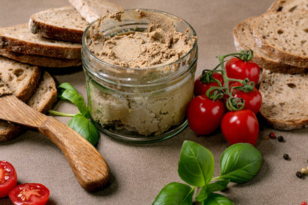 Homemade liver pate in glass jar with bread slices cherry tomatoes fresh basil leaves and wooden spoon. Healthy appetizer for breakfast or snack.の写真素材