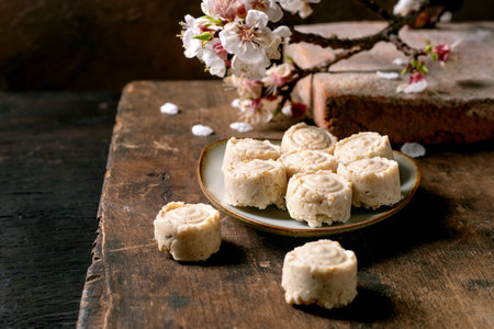 Traditional Asian dessert sweets sesame cream candies on ceramic plate. Wooden rustic table decorated with cherry blossom branch. Homemade rice flour confectionery rolls.の写真素材