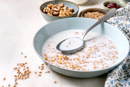 Bowl of sprouted wheat with milk with grains spoon. Small bowls of walnuts seeds and dried berries. Healthy breakfast concept clean eating nutritious meal.の写真素材