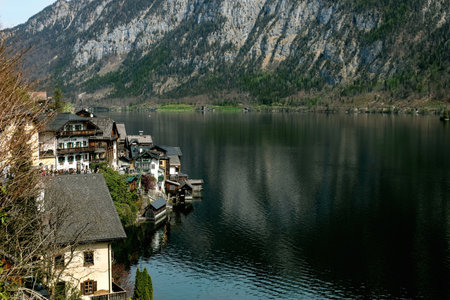 Picturesque Hallstatt village buildings nestled along Hallstatt Lake shore with majestic Austrian Alps mountains background. Traditional European architecture reflects in calm water.の写真素材