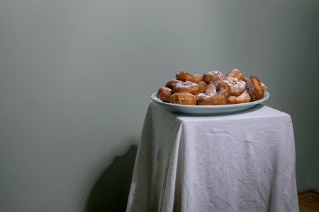 Fresh homemade donuts dusted with powdered sugar served on a plate. Minimalist composition with white tablecloth against neutral background.の写真素材