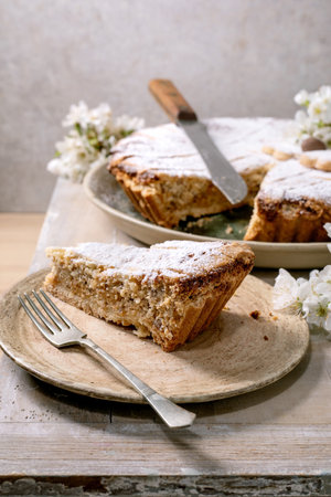 Homemade pie Pastiera Napolitano slice with powdered sugar on ceramic plate. Serving knife fork white flowers. Rustic wooden background. Delicious dessert.の写真素材