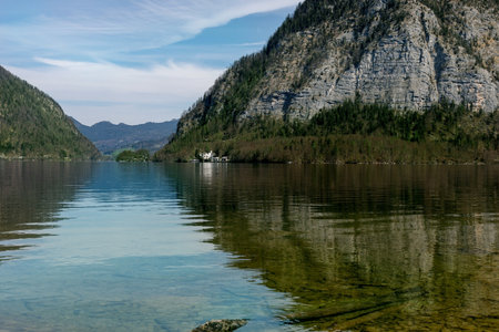 Hallstatt Austria. Serene alpine lake surrounded by steep mountain ranges reflecting in clear turquoise water. Small settlement visible at shoreline. Landscape nature scene for travel destination.の写真素材