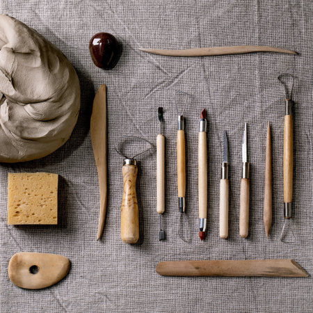 Set for pottery hobby. Piece of raw gray clay and kit of pottery ceramics tools in row on linen fabric cloth. Top view. DIY potter hobbyの写真素材