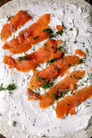 Fresh smoked salmon slices on cream cheese spread over flatbread garnished with chopped dill herbs rustic preparation processの写真素材