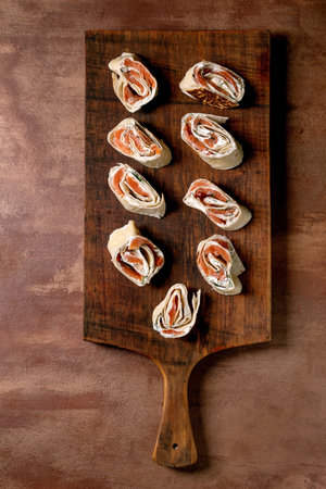 Delicious salmon cream cheese wraps served appetizers on rustic wooden cutting board against brown background. Perfect for party snack or buffet.の写真素材