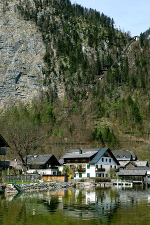 Hallstatt Austria. Traditional houses lake shore mountain backdrop Alps. Charming waterfront settlement surrounded by steep rocky cliffs covered with evergreen forest. Peaceful rural landscapeの写真素材
