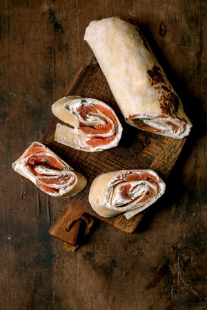 Sliced salmon wrap with cream cheese herbs on rustic wooden cutting board. Fresh appetizer with fish cream filling.の写真素材