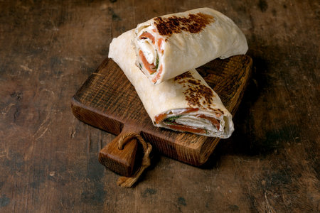 Fresh salmon tortilla wraps with cream cheese herbs on vintage wooden cutting board. Homemade appetizer on rustic table background.の写真素材