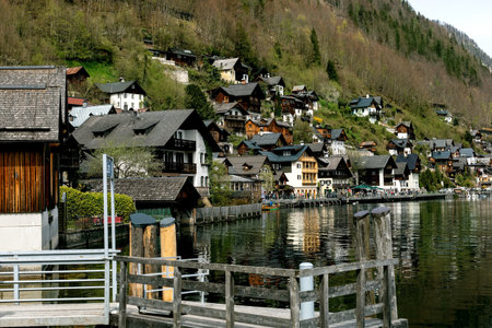 Hallstatt Austria. Scenic view of traditional wooden alpine houses nestled on hillside overlooking lake in Hallstatt Austria. Traditional architecture reflects in calm water wooden pier foreground.の写真素材