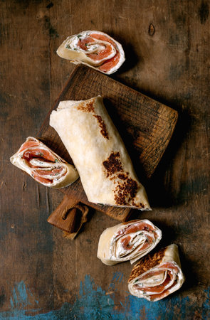 Homemade salmon cream cheese wrap cut into pieces on rustic wooden cutting board. Traditional appetizer made with smoked salmon soft cheese and herbs.の写真素材
