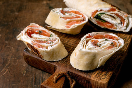 Delicious salmon and cream cheese wraps sliced on rustic wooden cutting board. Fresh tortilla rolls with herbs perfect appetizer for parties.の写真素材
