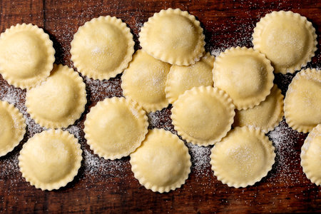 Handmade ravioli pasta arranged on floured wooden cutting board. Traditional Italian cuisine preparation showing raw dumplings ready for cooking.の写真素材