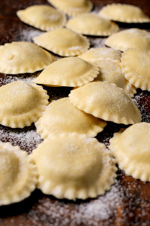 Fresh homemade ravioli pasta scattered with flour on wooden cutting board. Traditional Italian cuisine preparation process.の写真素材