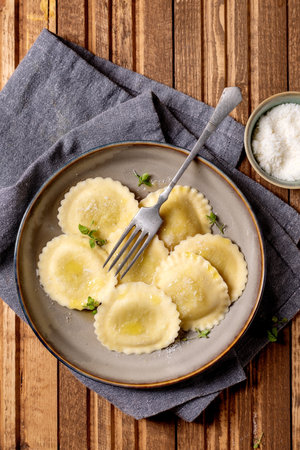 Delicious homemade ravioli pasta served on ceramic plate with fork parmesan cheese herbs on wooden table backgroundの写真素材