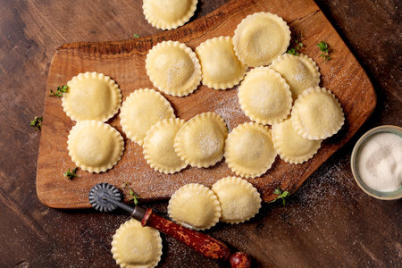 Top view fresh homemade ravioli pasta on wooden cutting board with flour and kitchen utensilsの写真素材