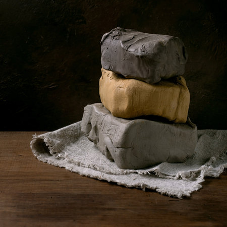 Three pieces of raw clay of different colors in stack, including gray and yellow, on a wooden table with a dark background. A concept for ceramic supplies stores and pottery workshops. Copy spaceの写真素材