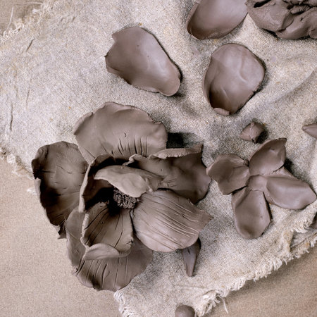 Creating a Clay Flower: DIY ceramic Workshop Idea. Petals and buds prepared for crafting magnolia flower from dark clay on rough fabric surface. Dark textured background, ceramicist's tools. Top view.の写真素材