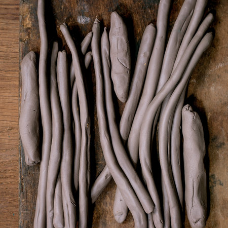 Pottery workshop preparation for children and adults: heap of raw clay ropes or sausages for work in coil technique on a dark wooden table. Top viewの写真素材