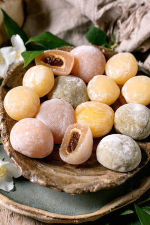 Colorful traditional Japanese mochi rice cakes with sweet filling on rustic wooden plate decorated with white flowers and green leavesの写真素材
